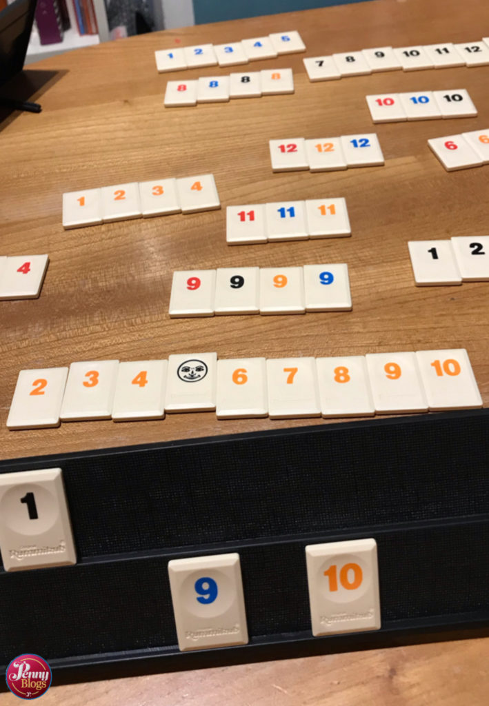 Rummikub tiles arranged in sets and runs on a table surface with a rack in the foreground of the picture