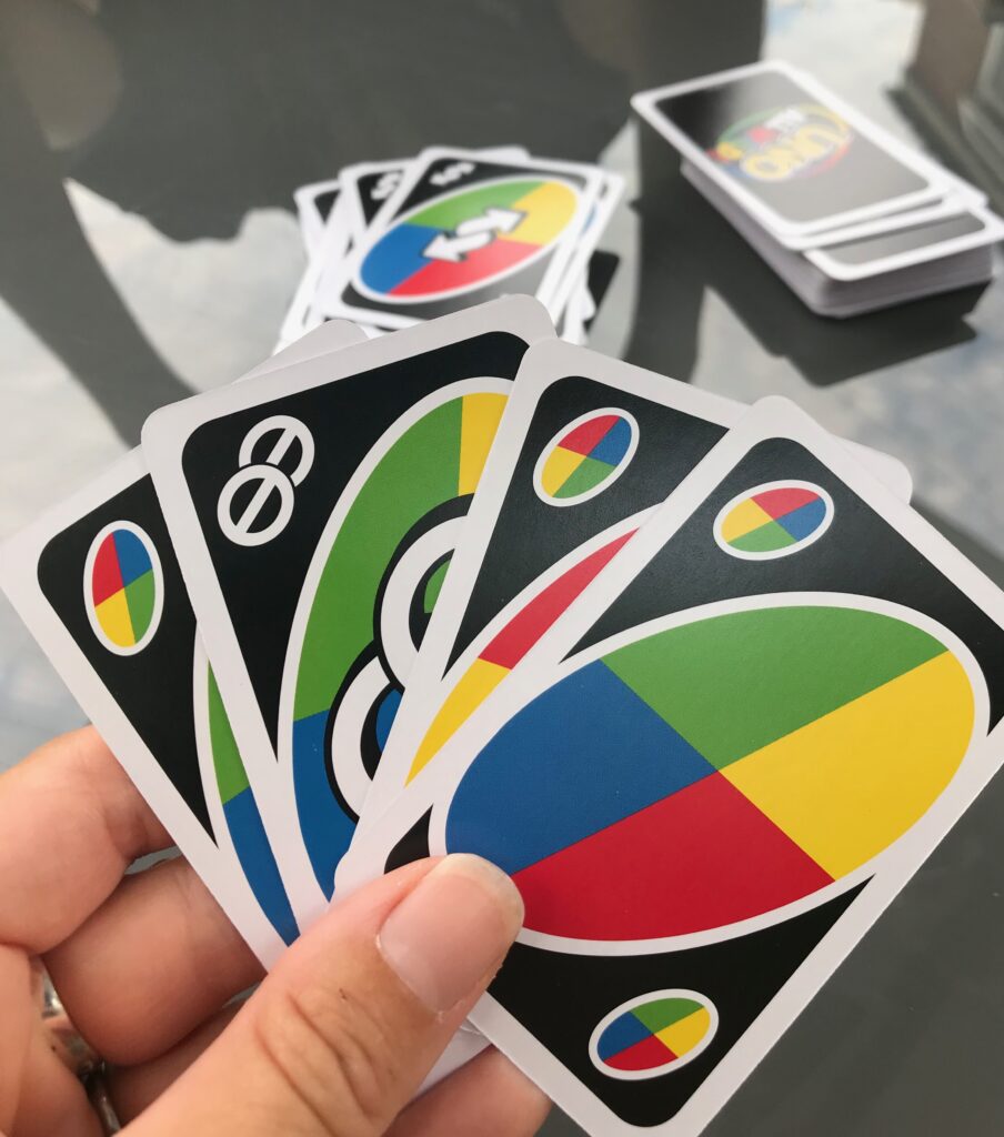 A game of Uno All Wild in progress. In the foreground is a hand containing mainly standard wild cards, but in amongst them is on skip two card. In the background you can see a draw and discard pile for the game.