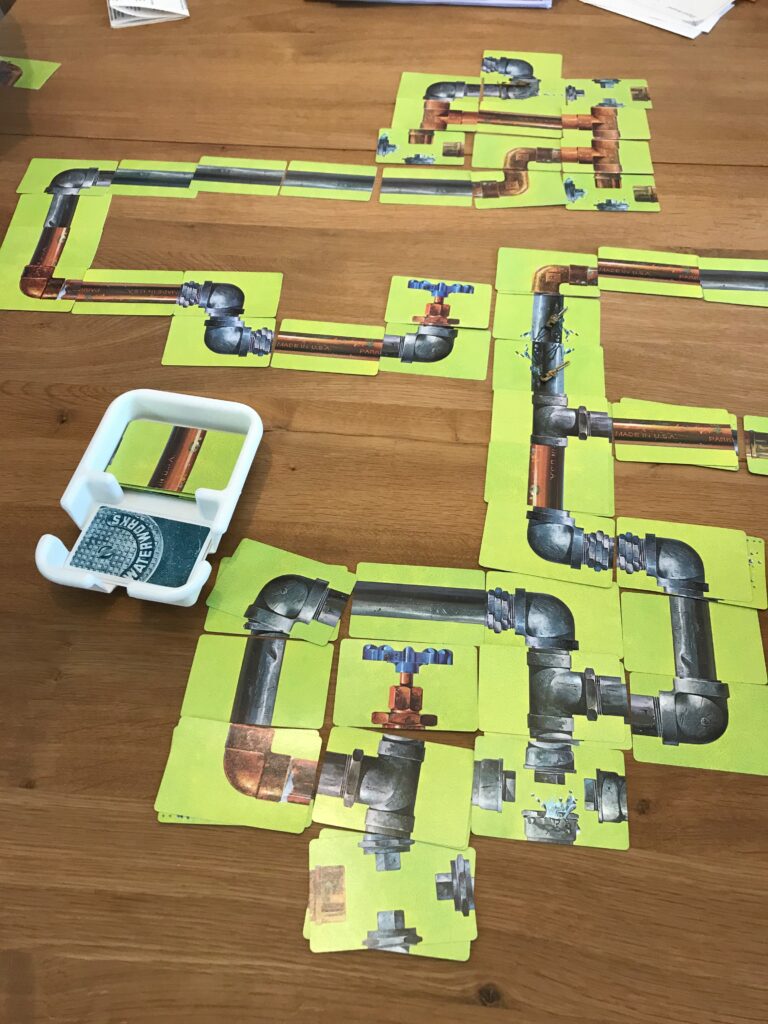 A top down view of a tangled mess of cards showing two players pipelines in the game waterworks.