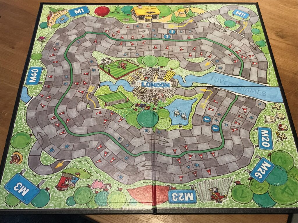 The M25 game board showing London in the middle of the board and two directions of the M25 looping round. The River Thames comes in from the right hand side of the board and the motorway goes into a tunnel under it. There are various slip roads and roundabouts for junctions with other motorways and cartoon versions of some famous 1980s landmarks.