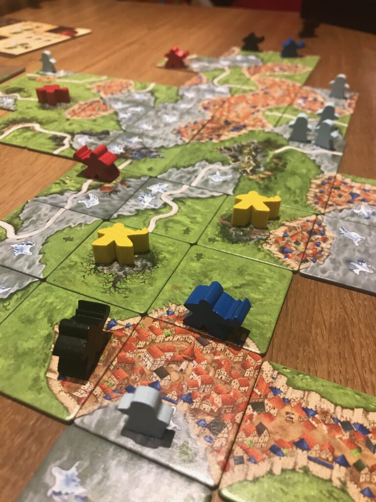 Tiles in the game particularly showing two buried meeples on cemeteries - denoted by two lying down meeples on these tiles which are both surrounded on four sides by other tiles.