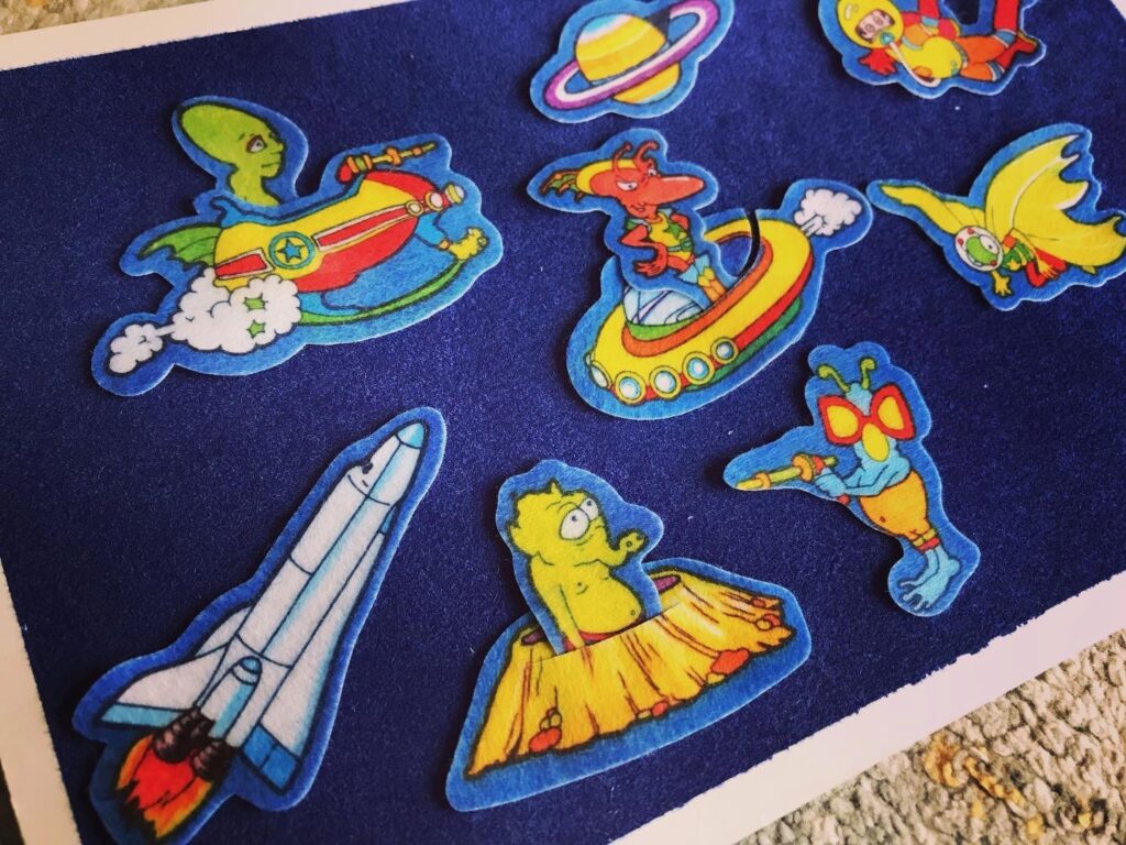 A fuzzy felt scene showing a variety of aliens and other creatures in shape ships and firing guns at each other, all on a dark blue background.