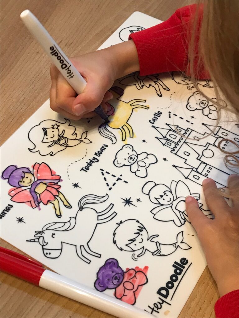 An arms is in shot colouring in a unicorn on a Hey Doodle colouring mat.
