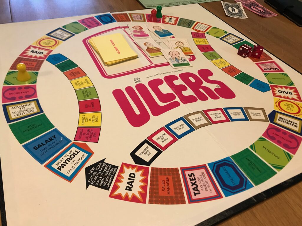 The board of Ulcers. There is a white background to the board and a main circular track of squares. Off it are three smaller tracks that appear as arcs inside the circle.