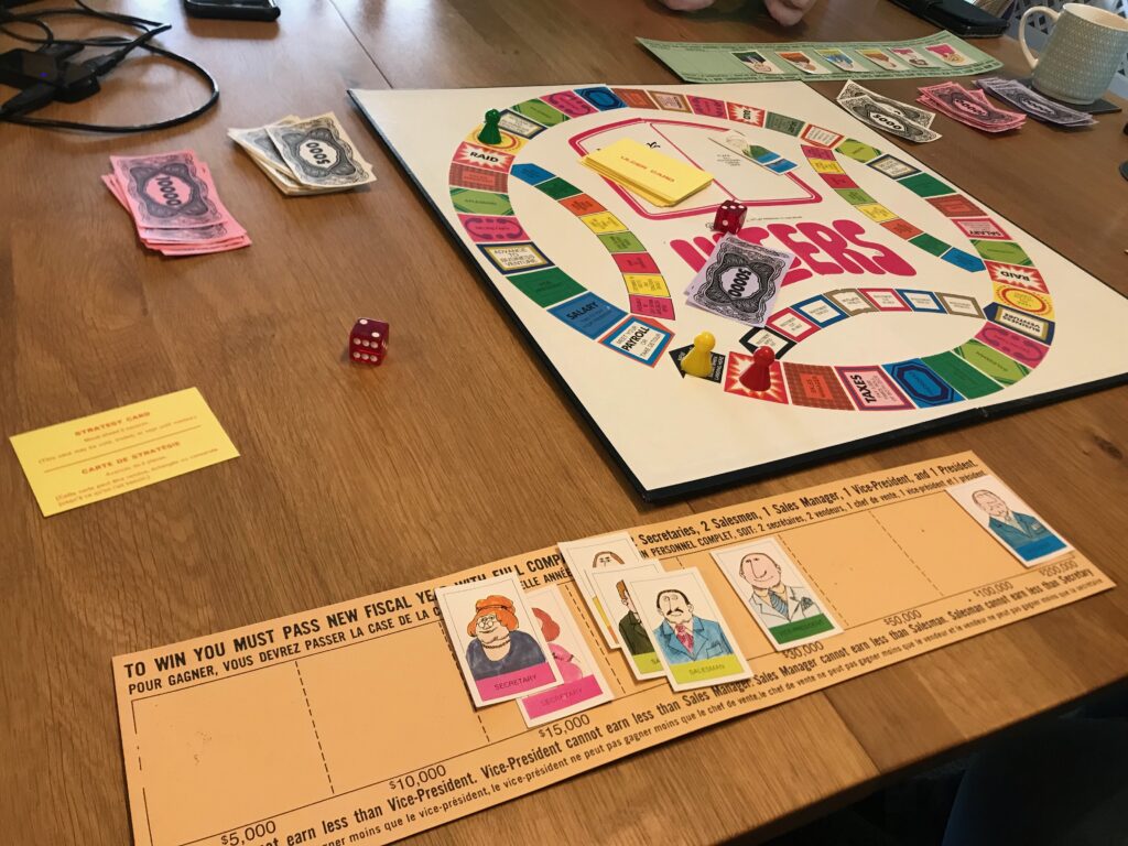 A view of the table as we played the game. Visible in the foreground is my company board with seven staff members on it. In the background you can see an opponents company board with only six members of staff on it. Also on the table you can see money, dice and Ulcers cards as well as a mug of tea.