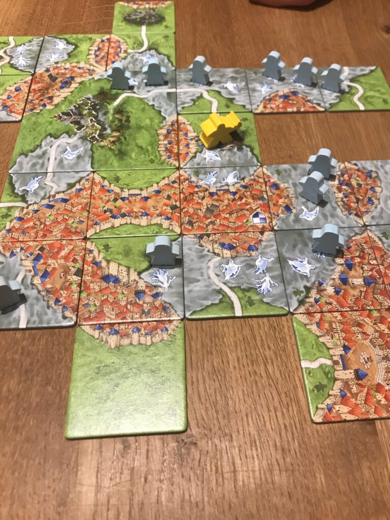 Tiles making up the game board of Mists over Carcassonne. Visible are several mist patches - some complete, some not. There are plenty of ghosts on the board, some completed cities and a yellow guard meeple stood on a section of road.